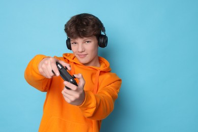 Photo of Teenage boy in headphones playing video game with controller on light blue background. Space for text