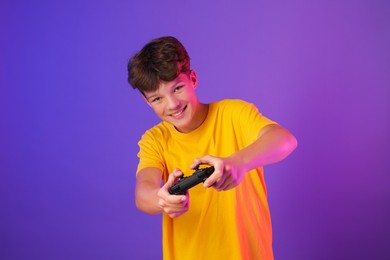 Happy teenage boy playing video game with controller on purple background