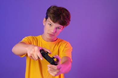 Teenage boy playing video game with controller on purple background. Space for text