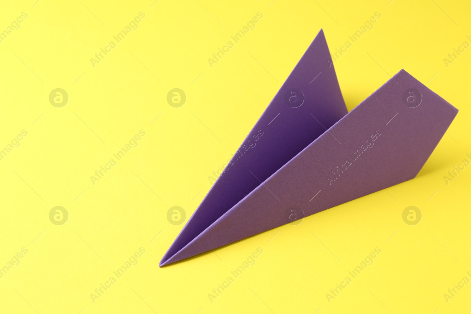 Photo of One handmade purple paper plane on yellow background, space for text