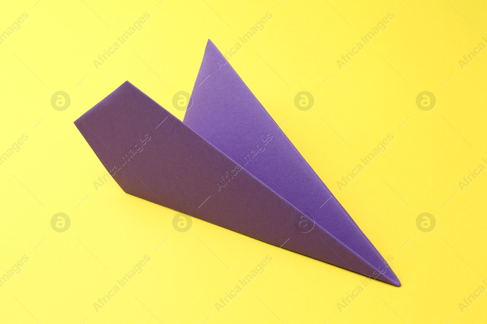 Photo of One handmade purple paper plane on yellow background