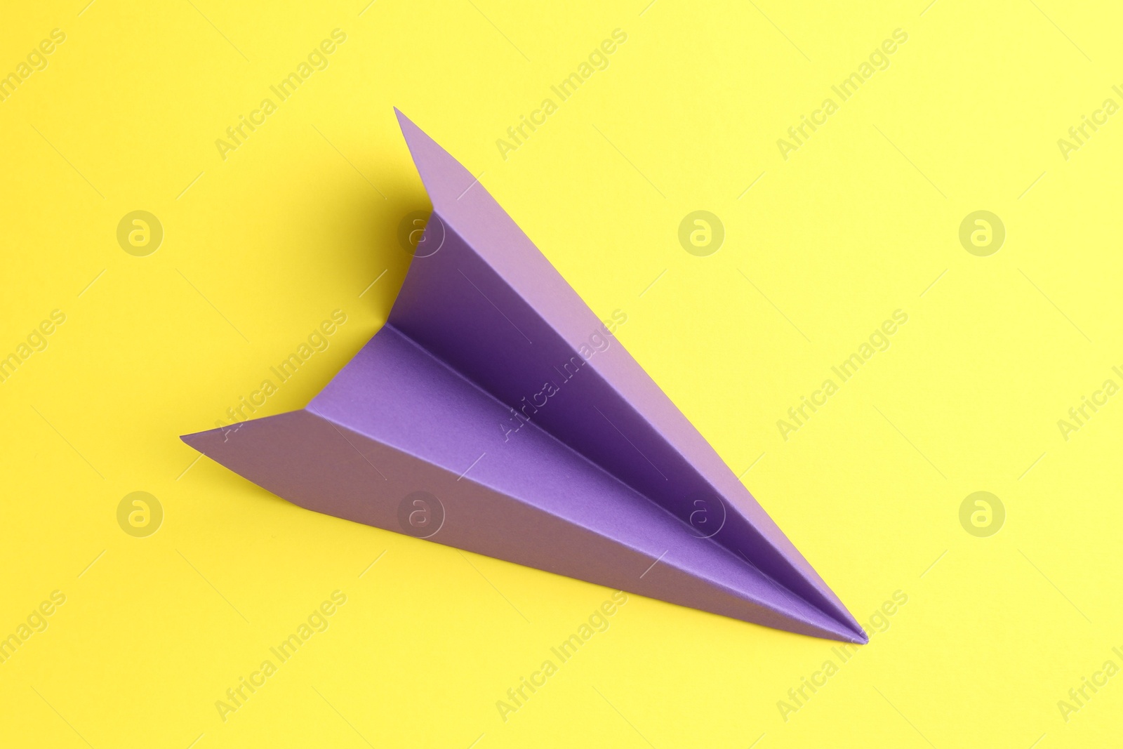 Photo of One handmade purple paper plane on yellow background, top view