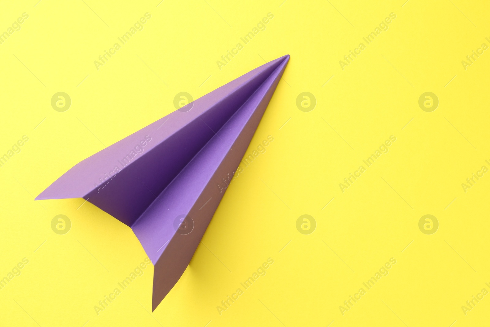 Photo of One handmade purple paper plane on yellow background, top view. Space for text