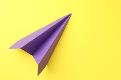 Photo of One handmade purple paper plane on yellow background, top view. Space for text