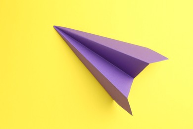 Photo of One handmade purple paper plane on yellow background, top view