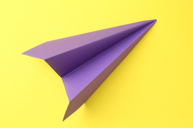 Photo of One handmade purple paper plane on yellow background, top view