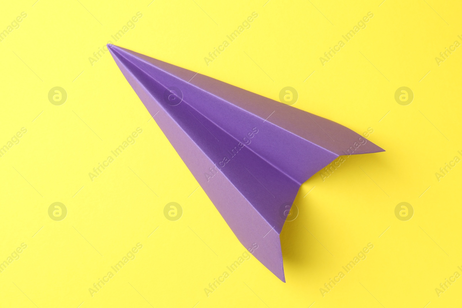 Photo of One handmade purple paper plane on yellow background, top view