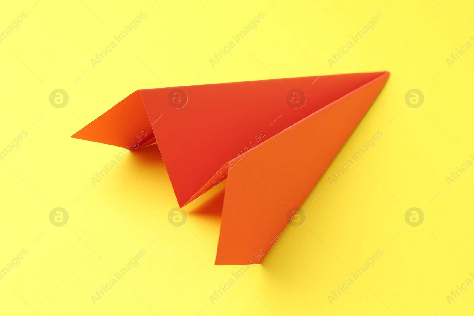 Photo of One handmade orange paper plane on yellow background