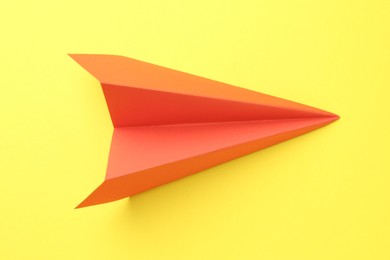 Photo of One handmade orange paper plane on yellow background, top view