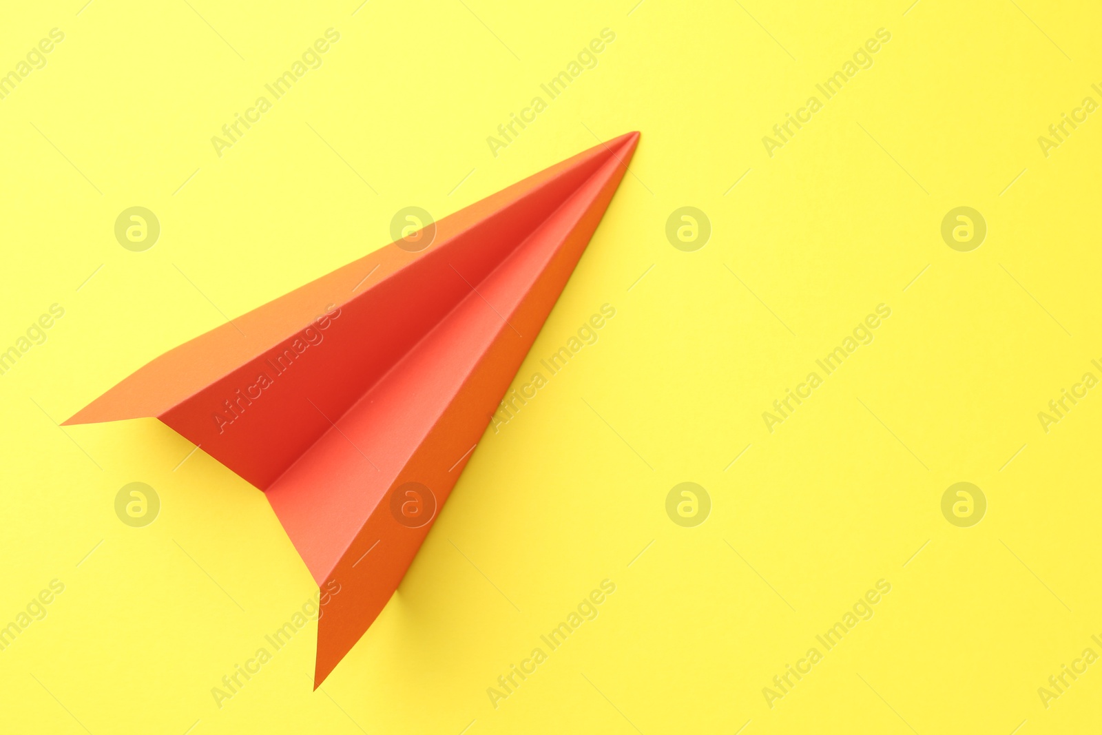 Photo of One handmade orange paper plane on yellow background, top view. Space for text