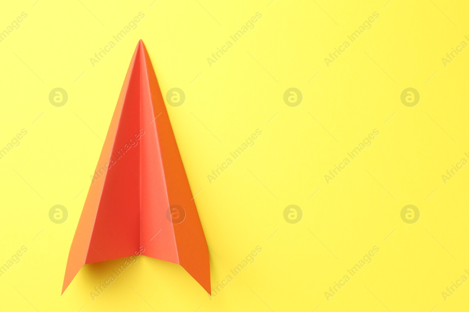 Photo of One handmade orange paper plane on yellow background, top view. Space for text