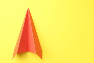 Photo of One handmade orange paper plane on yellow background, top view. Space for text