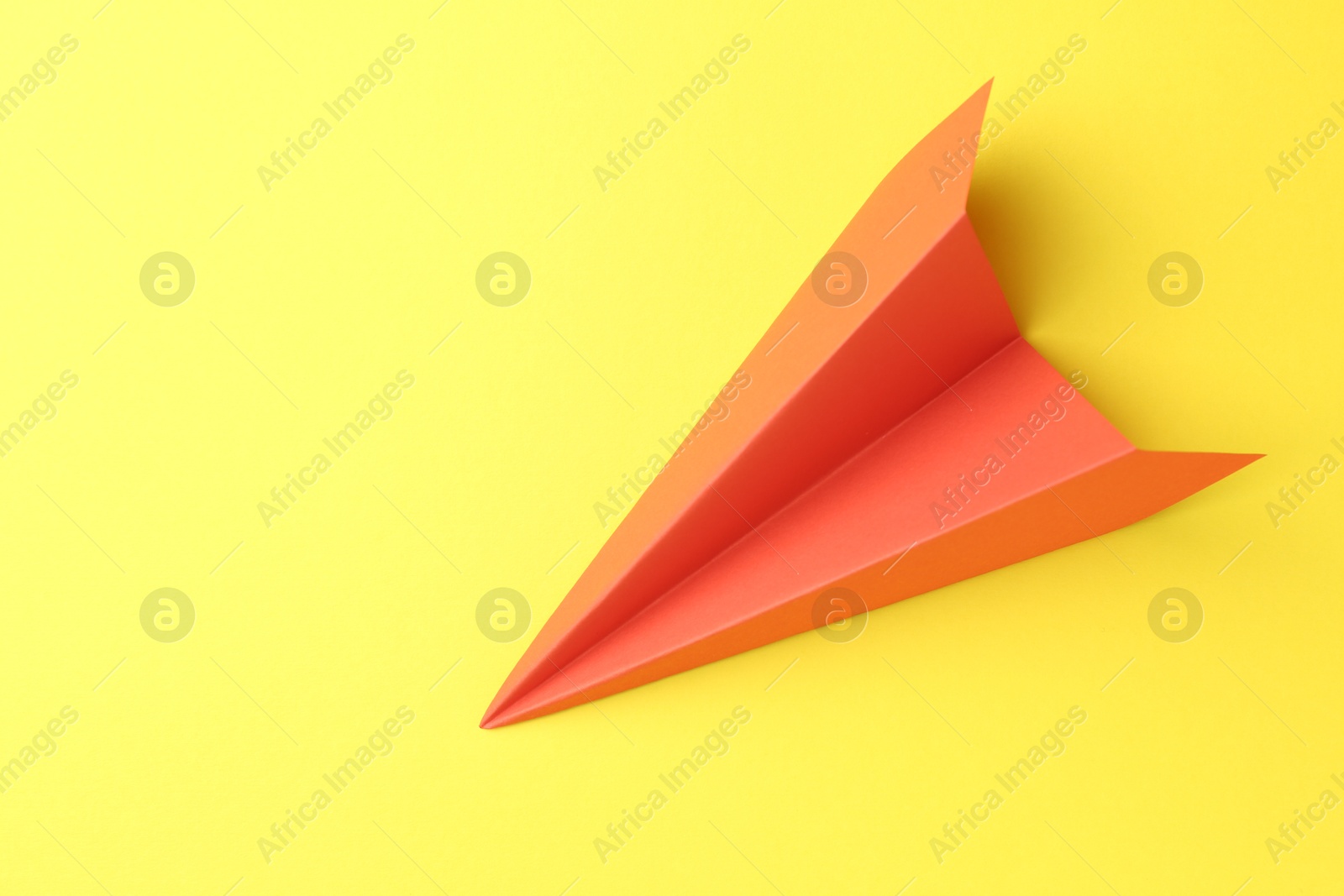 Photo of One handmade orange paper plane on yellow background, top view. Space for text