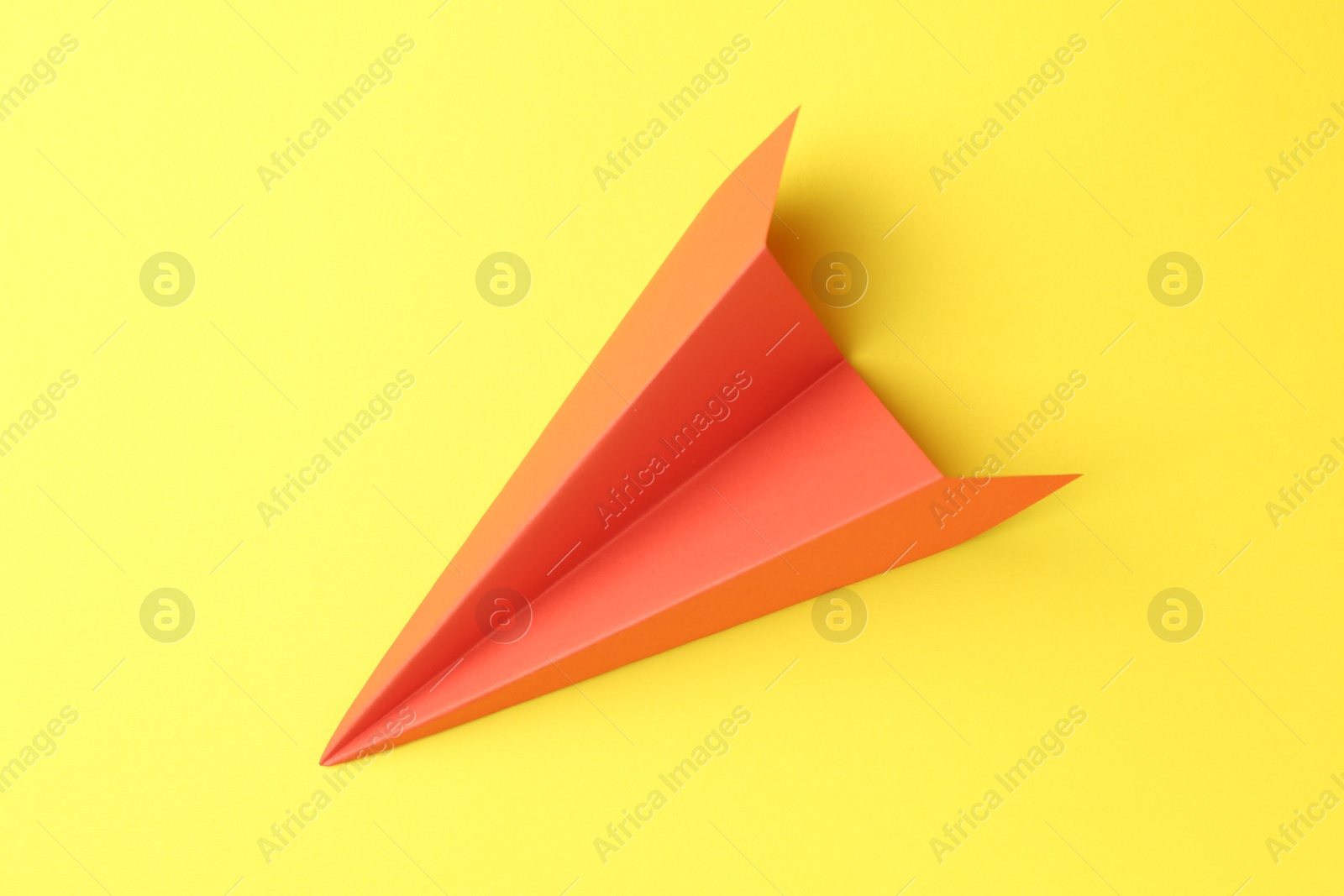 Photo of One handmade orange paper plane on yellow background, top view