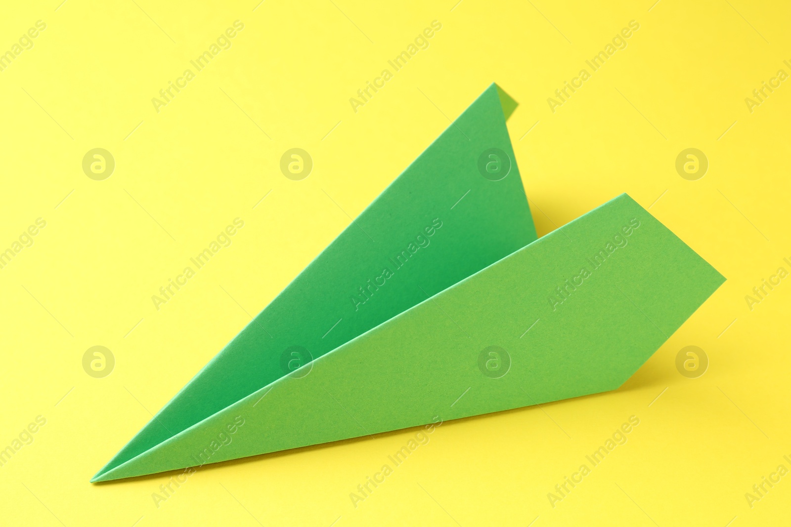 Photo of One handmade green paper plane on yellow background, closeup