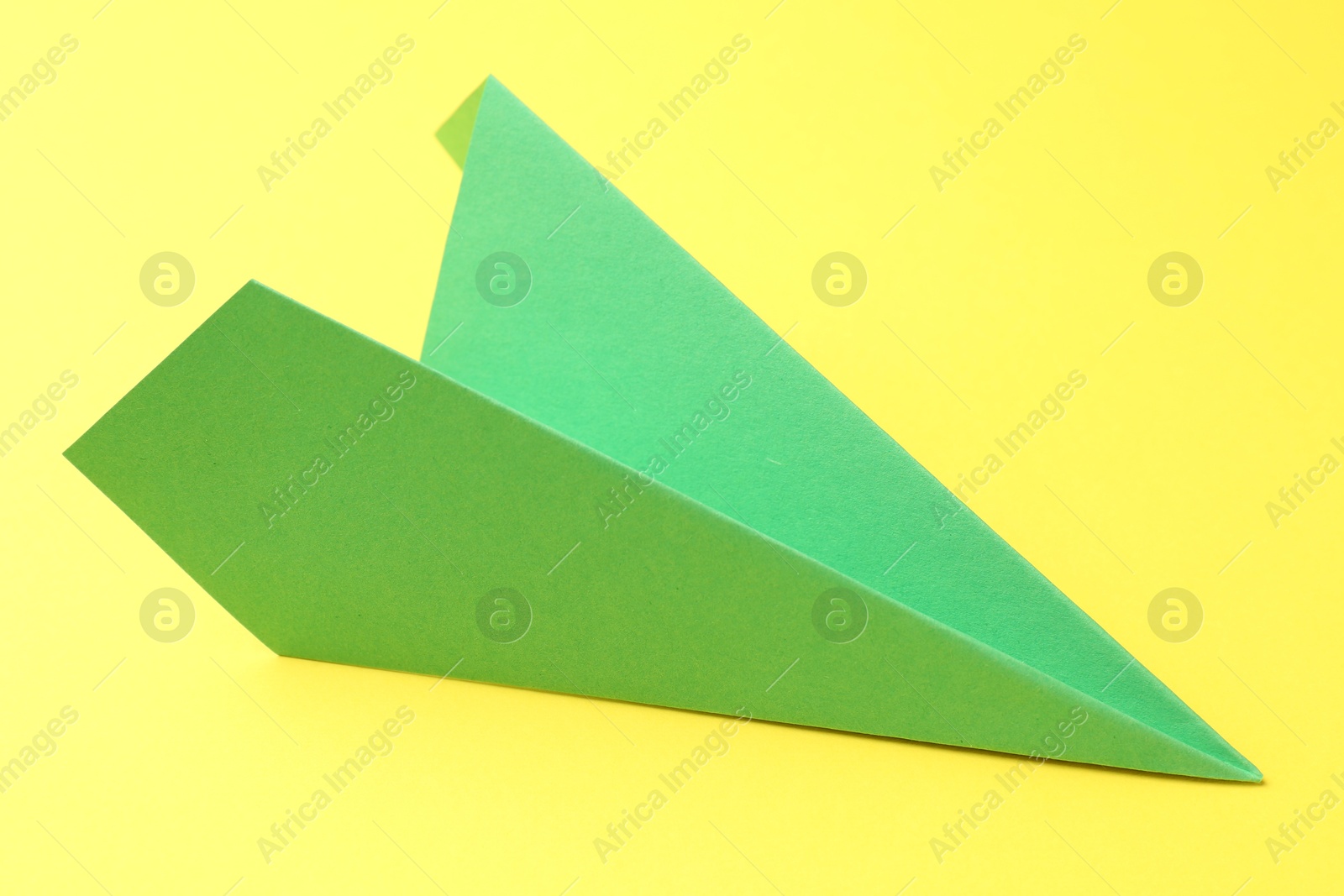 Photo of One handmade green paper plane on yellow background, closeup