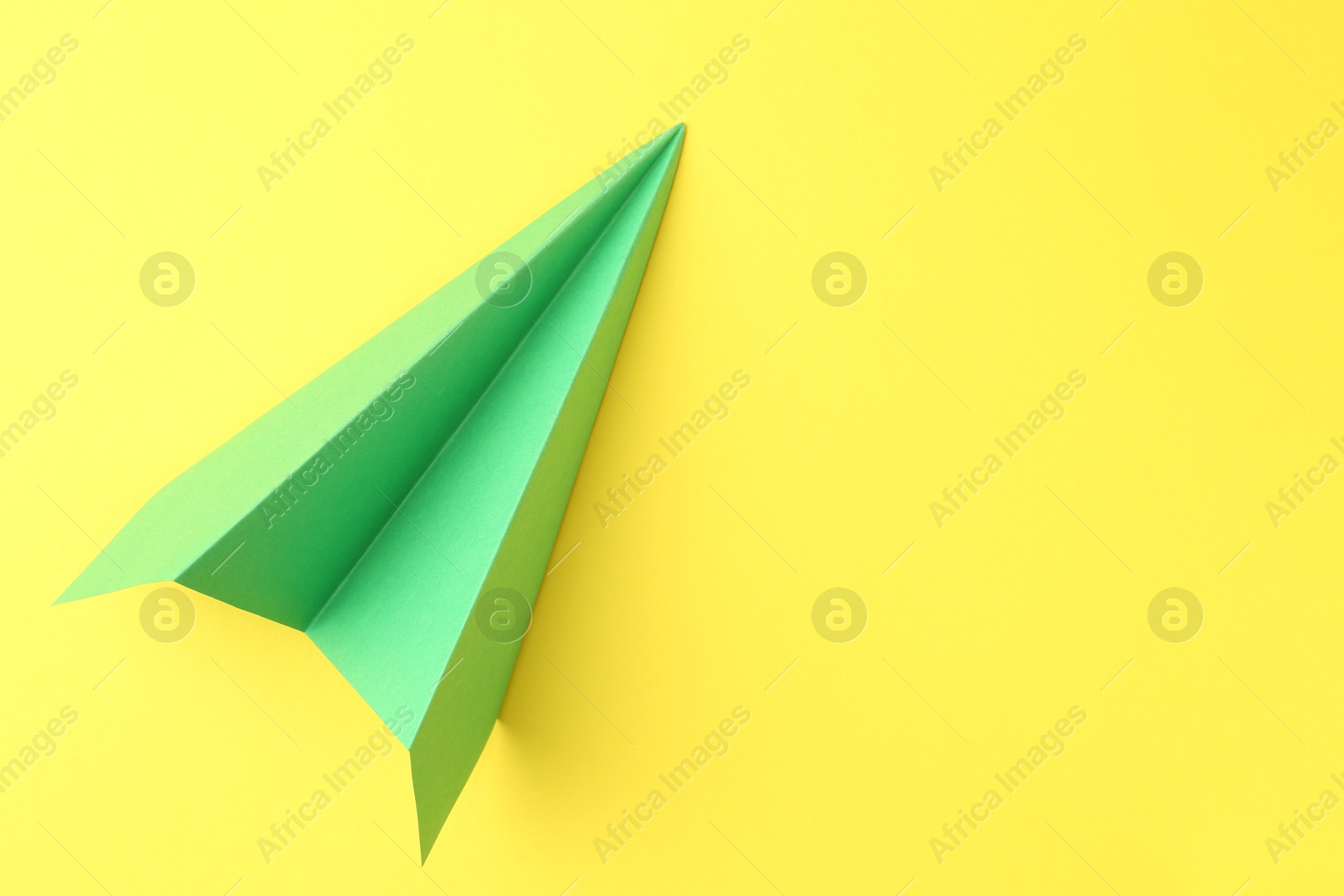 Photo of One handmade green paper plane on yellow background, top view. Space for text