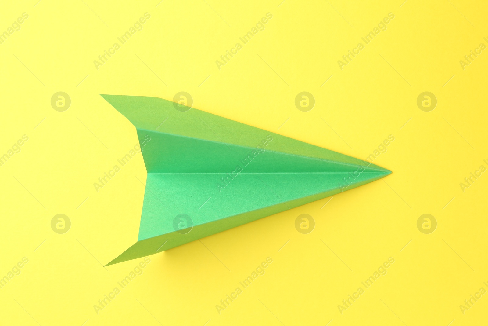 Photo of One handmade green paper plane on yellow background, top view