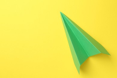 Photo of One handmade green paper plane on yellow background, top view. Space for text