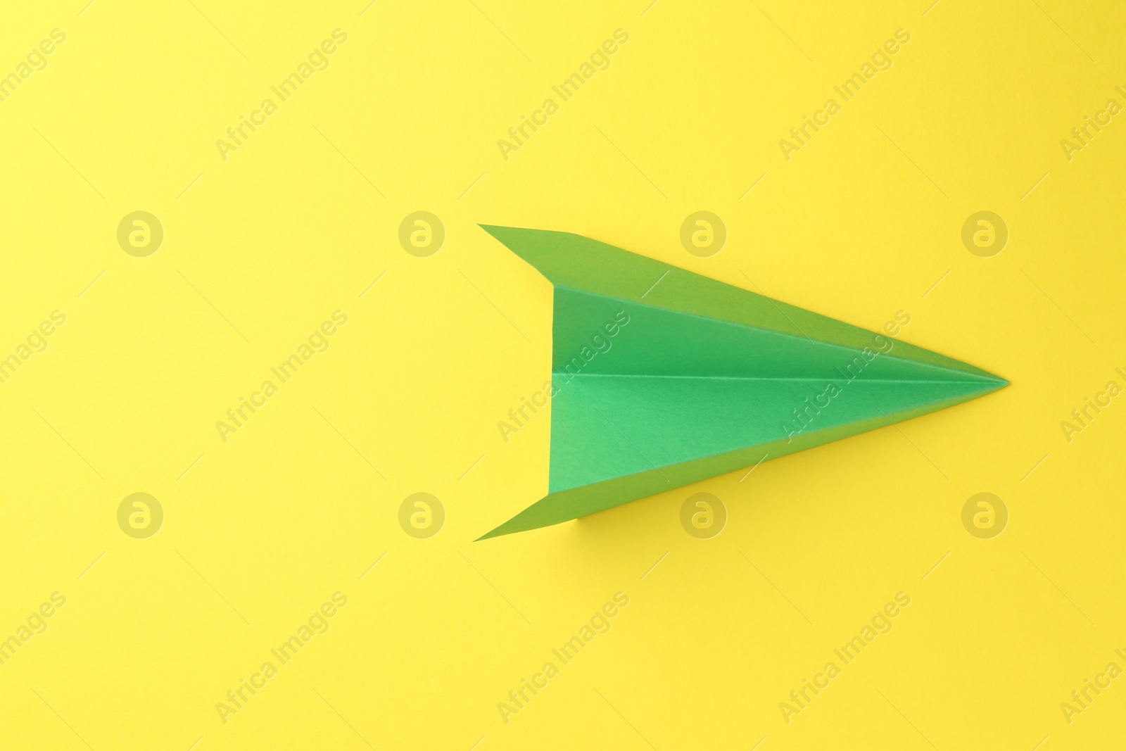 Photo of One handmade green paper plane on yellow background, top view. Space for text