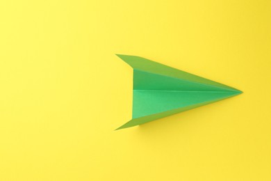 One handmade green paper plane on yellow background, top view. Space for text