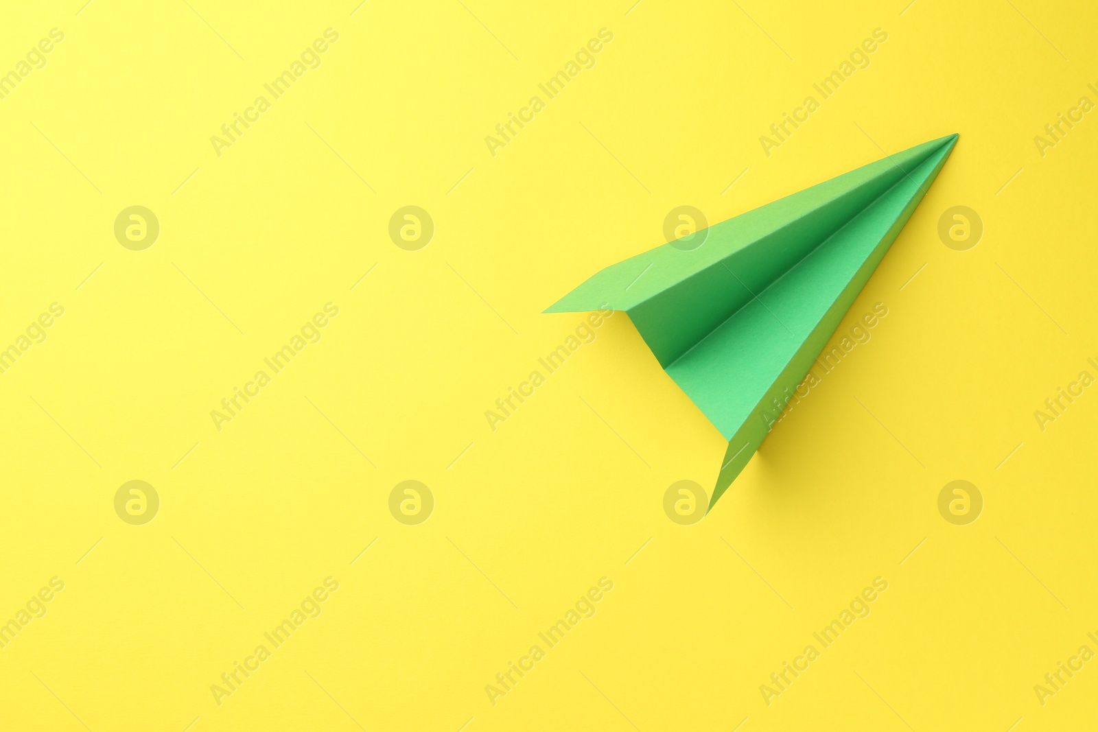 Photo of One handmade green paper plane on yellow background, top view. Space for text