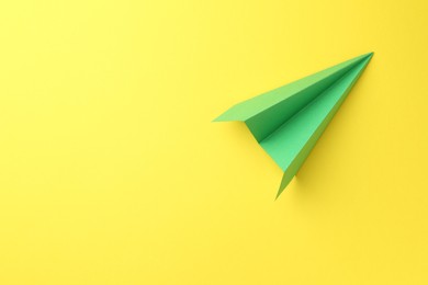 Photo of One handmade green paper plane on yellow background, top view. Space for text