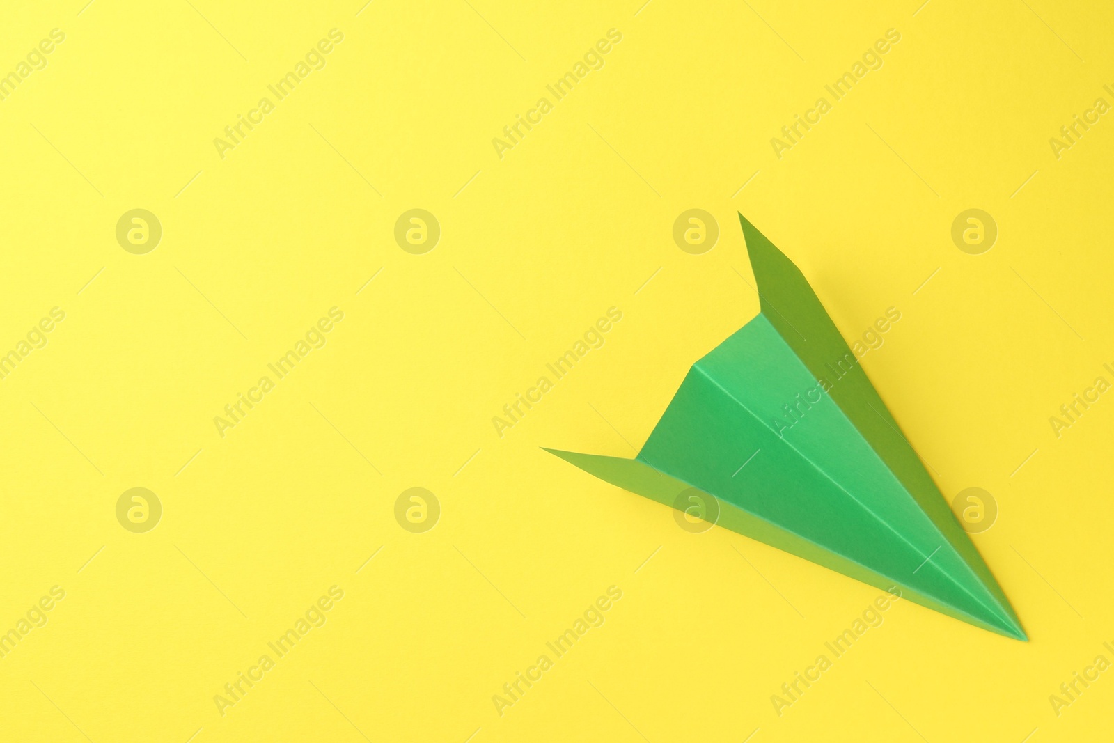 Photo of One handmade green paper plane on yellow background, top view. Space for text