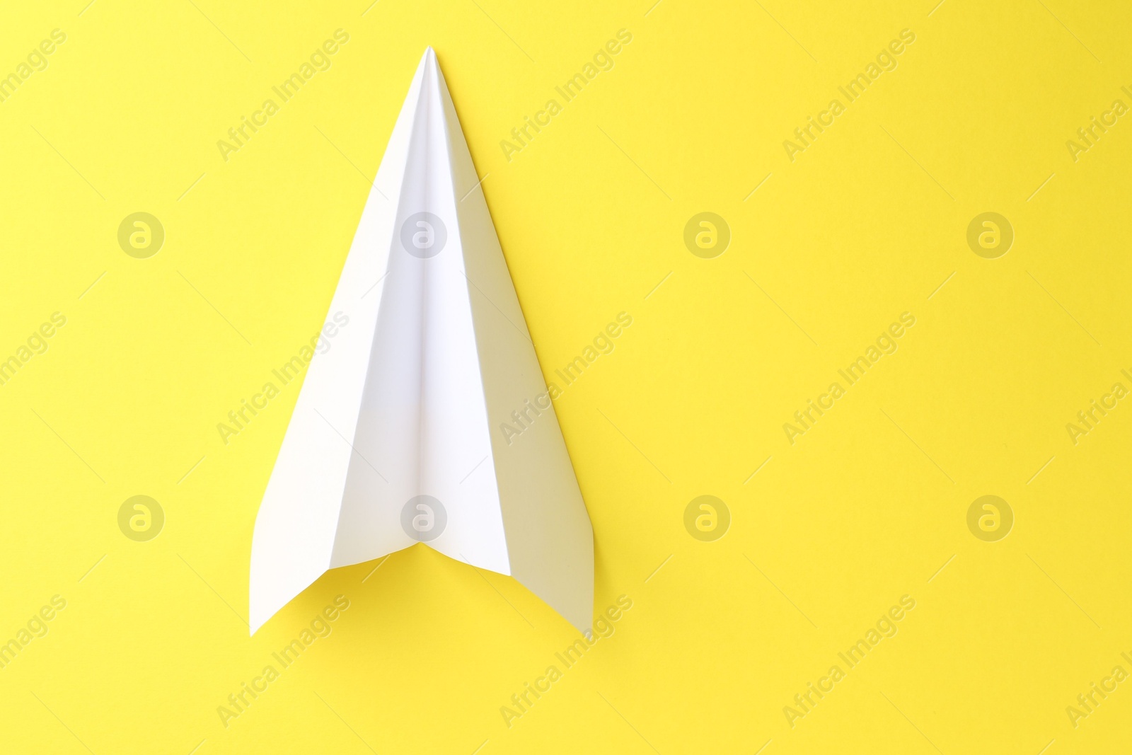 Photo of One handmade paper plane on yellow background, top view. Space for text