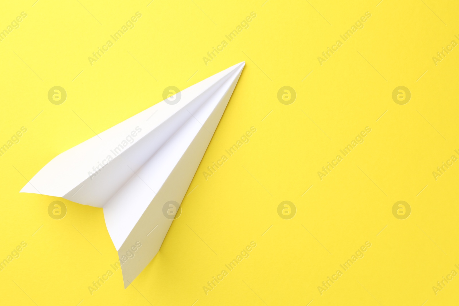 Photo of One handmade paper plane on yellow background, top view. Space for text