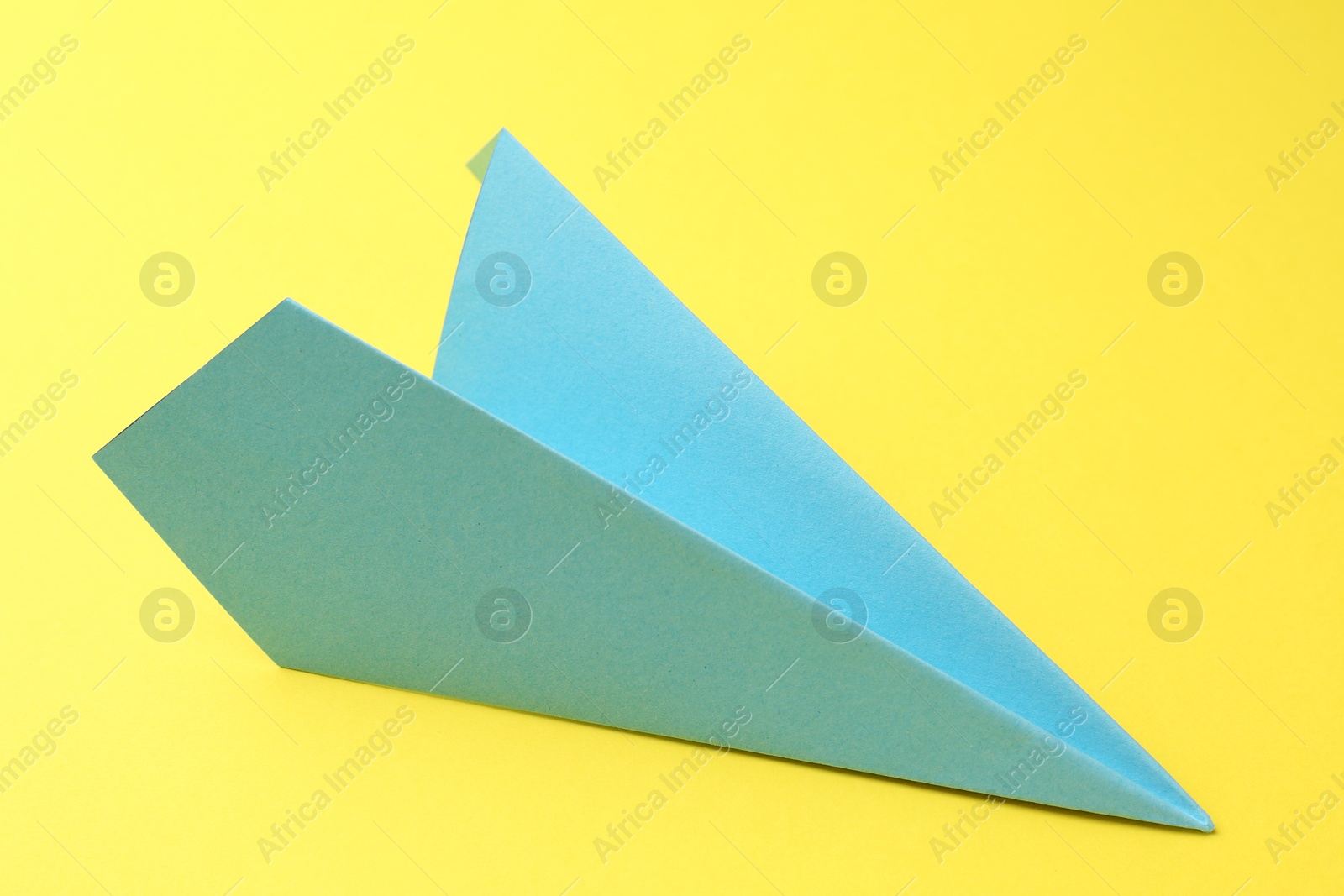 Photo of One handmade light blue paper plane on yellow background