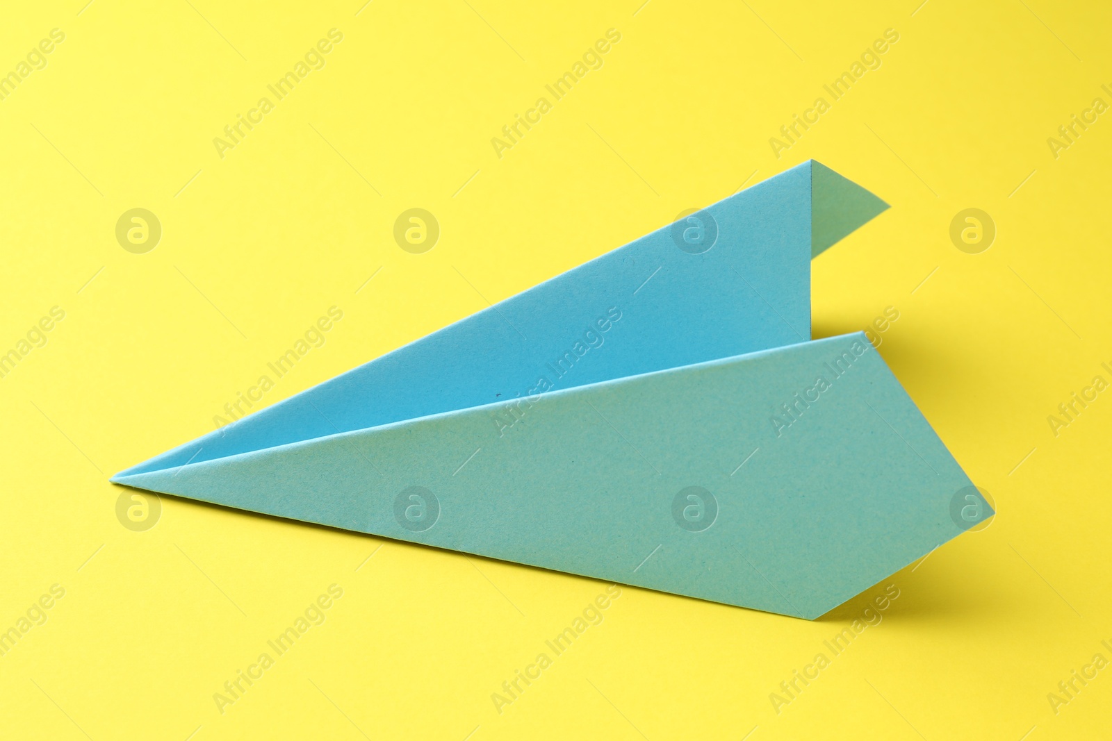 Photo of One handmade light blue paper plane on yellow background