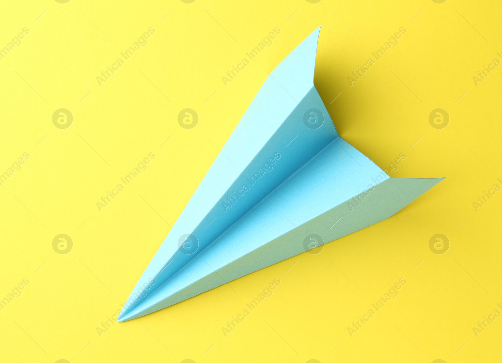 Photo of One handmade light blue paper plane on yellow background, top view