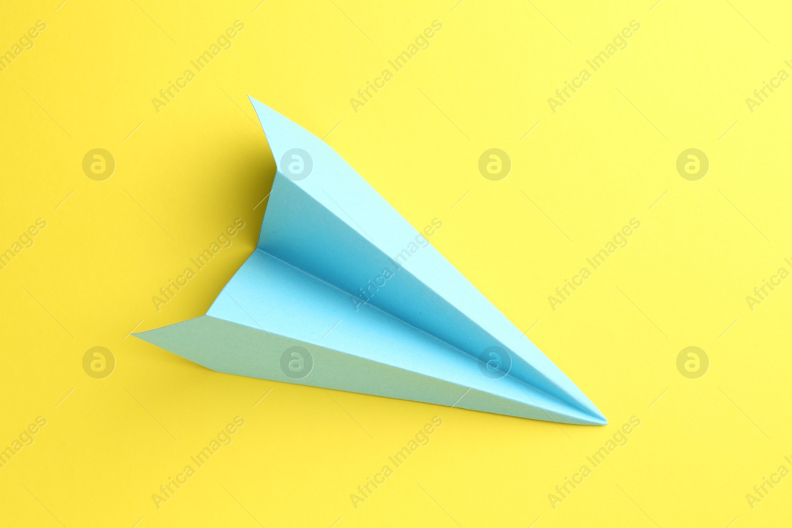 Photo of One handmade light blue paper plane on yellow background, top view