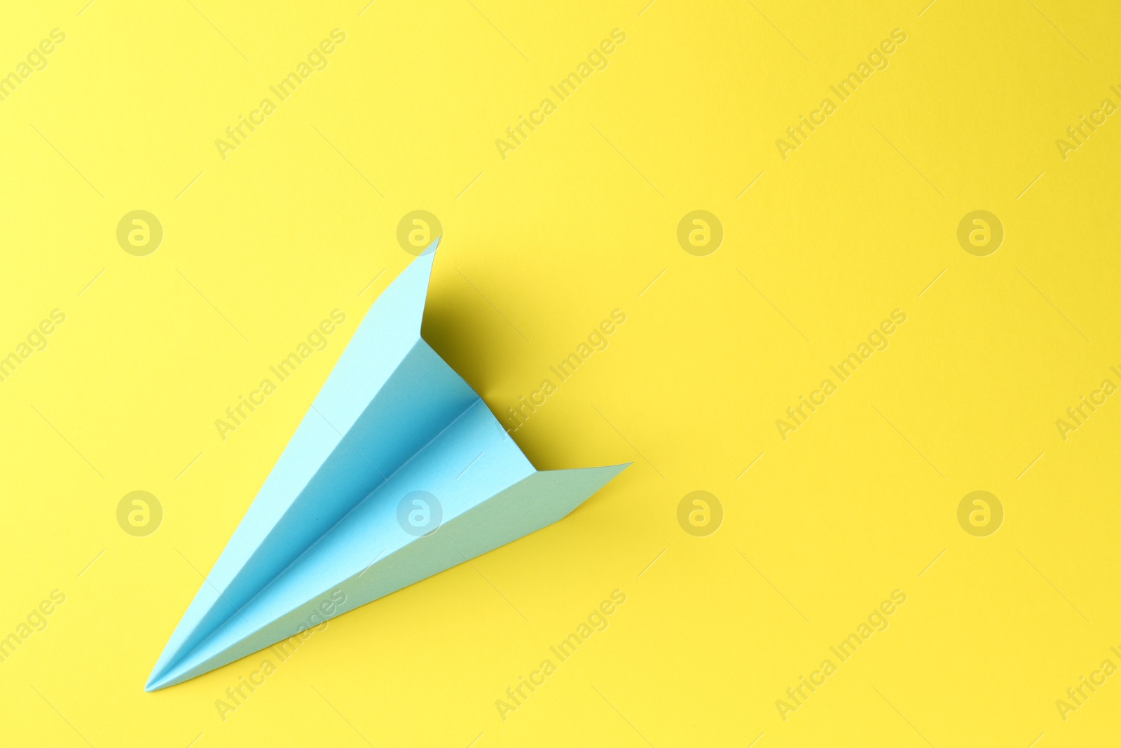 Photo of One handmade light blue paper plane on yellow background, top view. Space for text