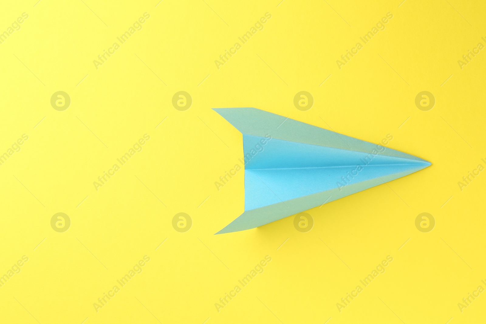 Photo of One handmade light blue paper plane on yellow background, top view. Space for text