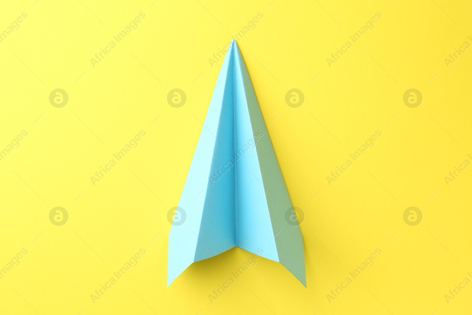 Photo of One handmade light blue paper plane on yellow background, top view