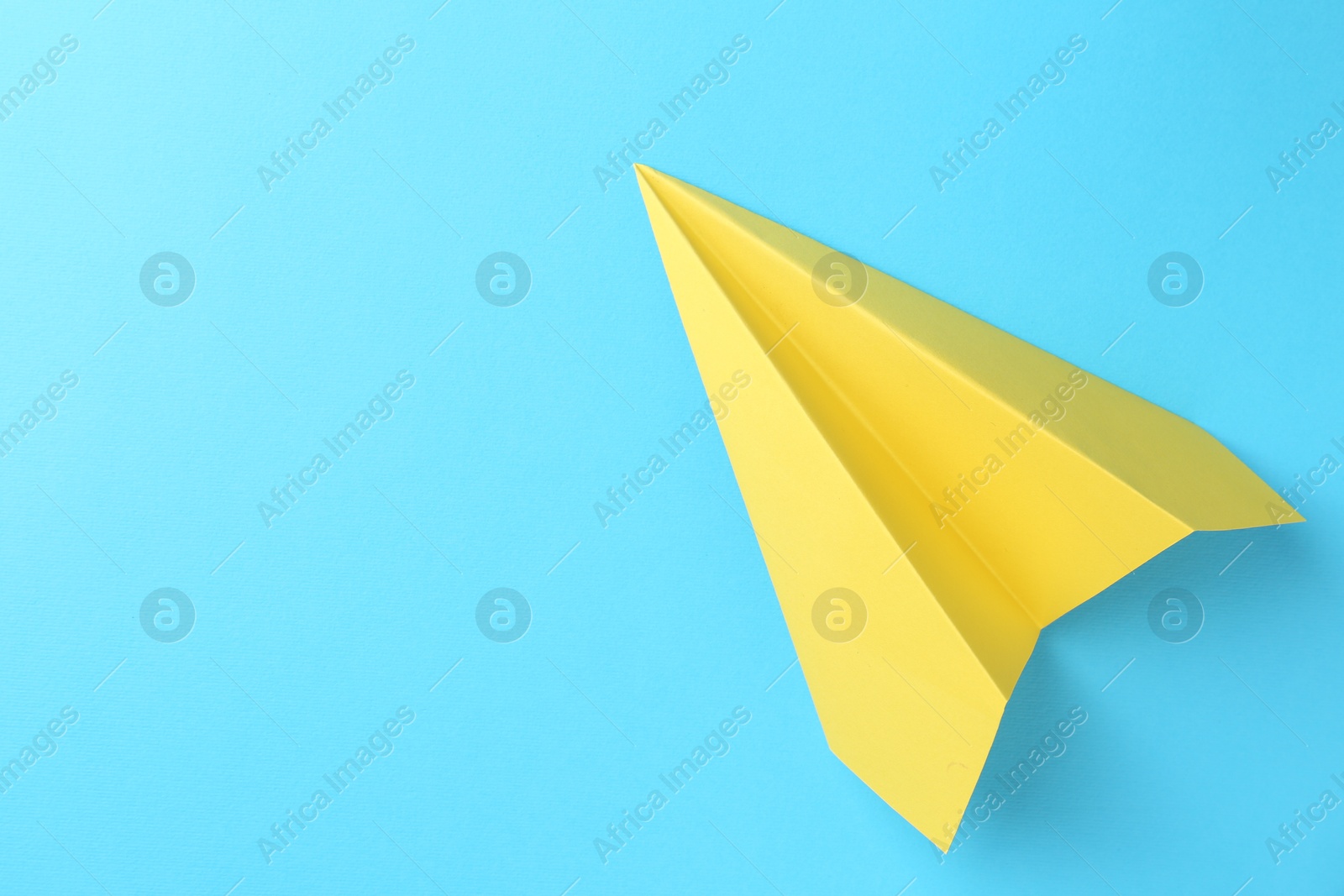 Photo of One handmade yellow paper plane on light blue background, top view. Space for text