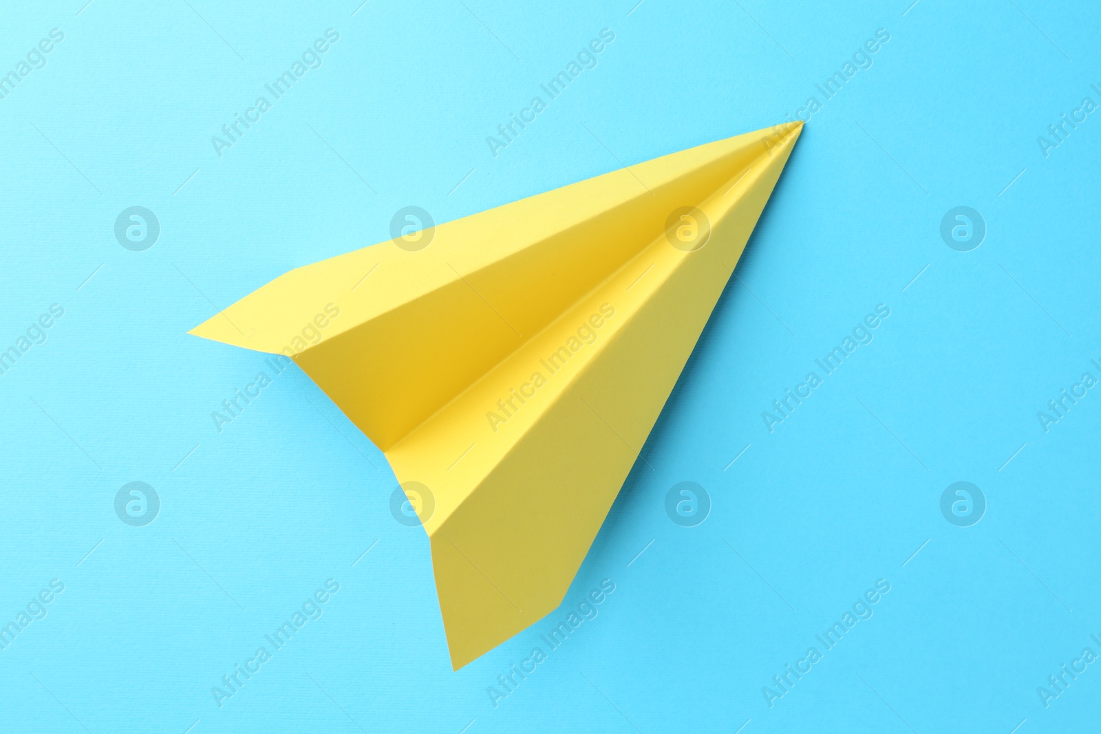 Photo of One handmade yellow paper plane on light blue background, top view