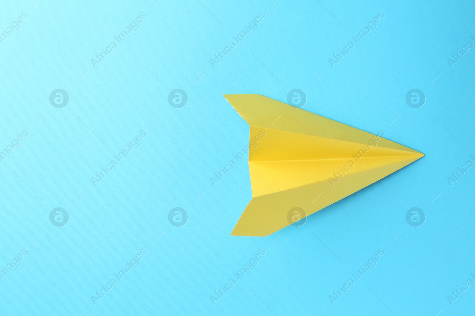 Photo of One handmade yellow paper plane on light blue background, top view. Space for text