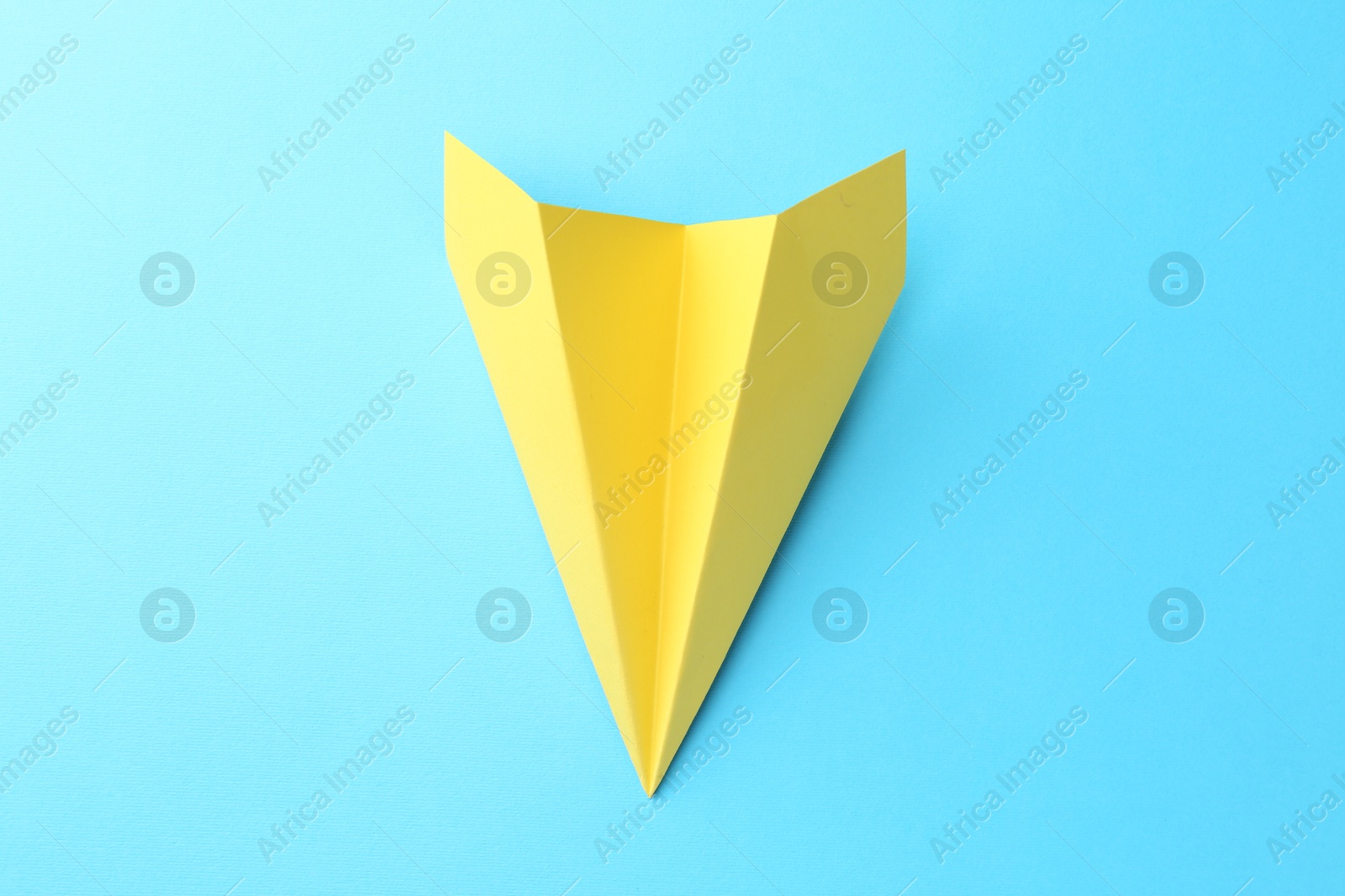 Photo of One handmade yellow paper plane on light blue background, top view