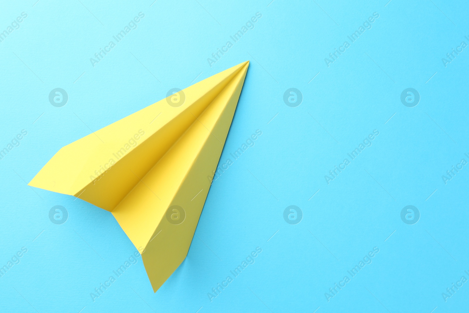 Photo of One handmade yellow paper plane on light blue background, top view. Space for text