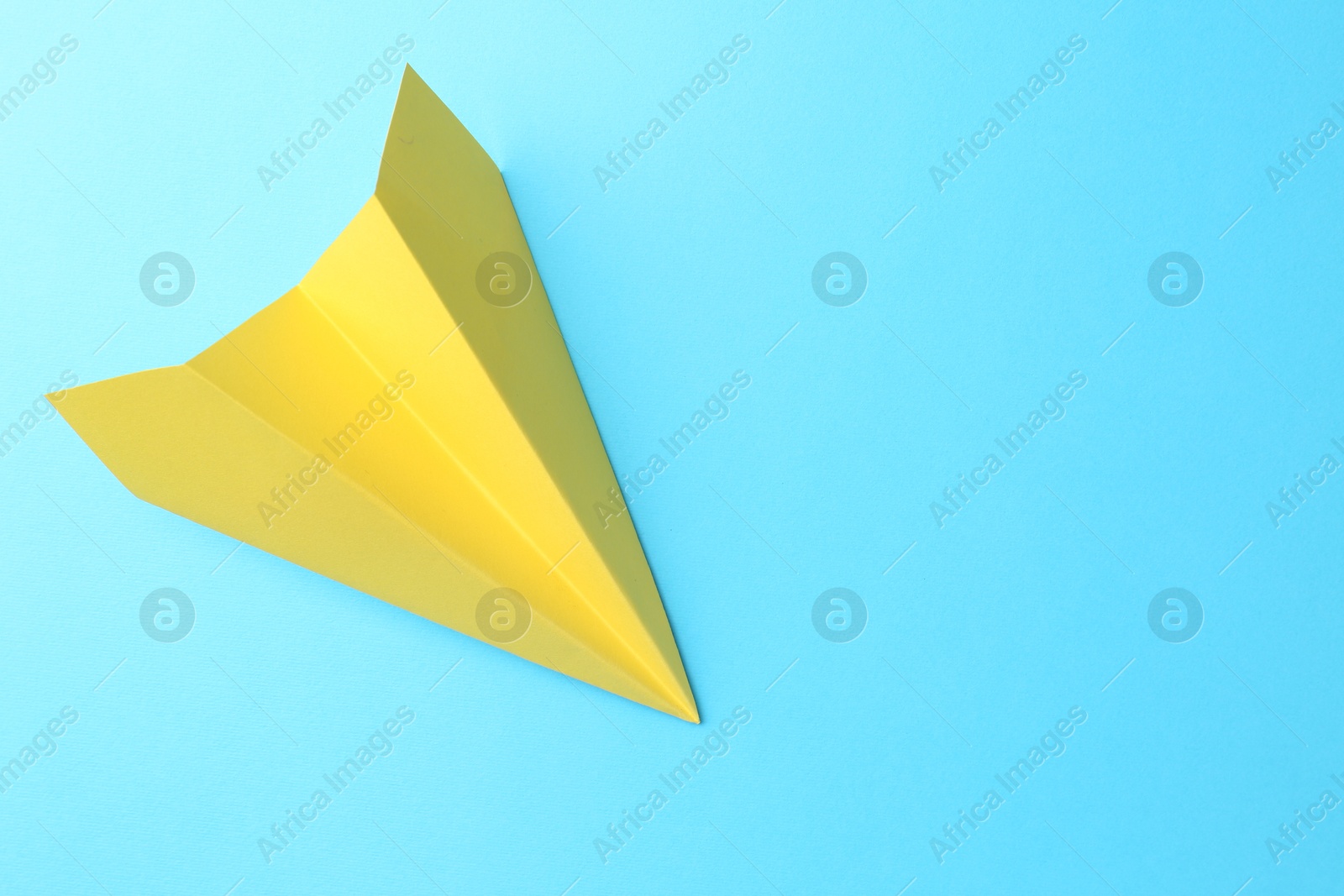 Photo of One handmade yellow paper plane on light blue background, top view. Space for text