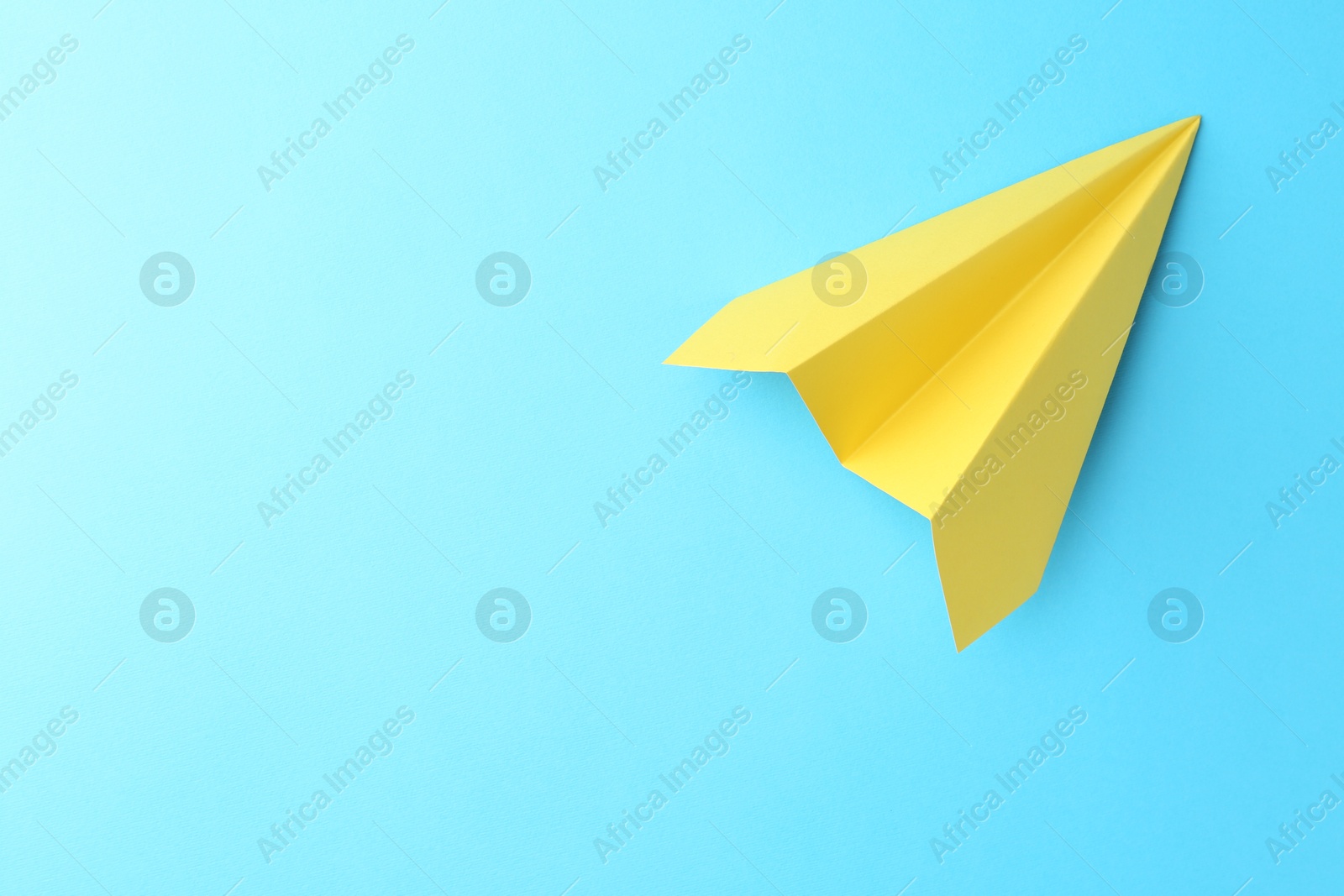 Photo of One handmade yellow paper plane on light blue background, top view. Space for text