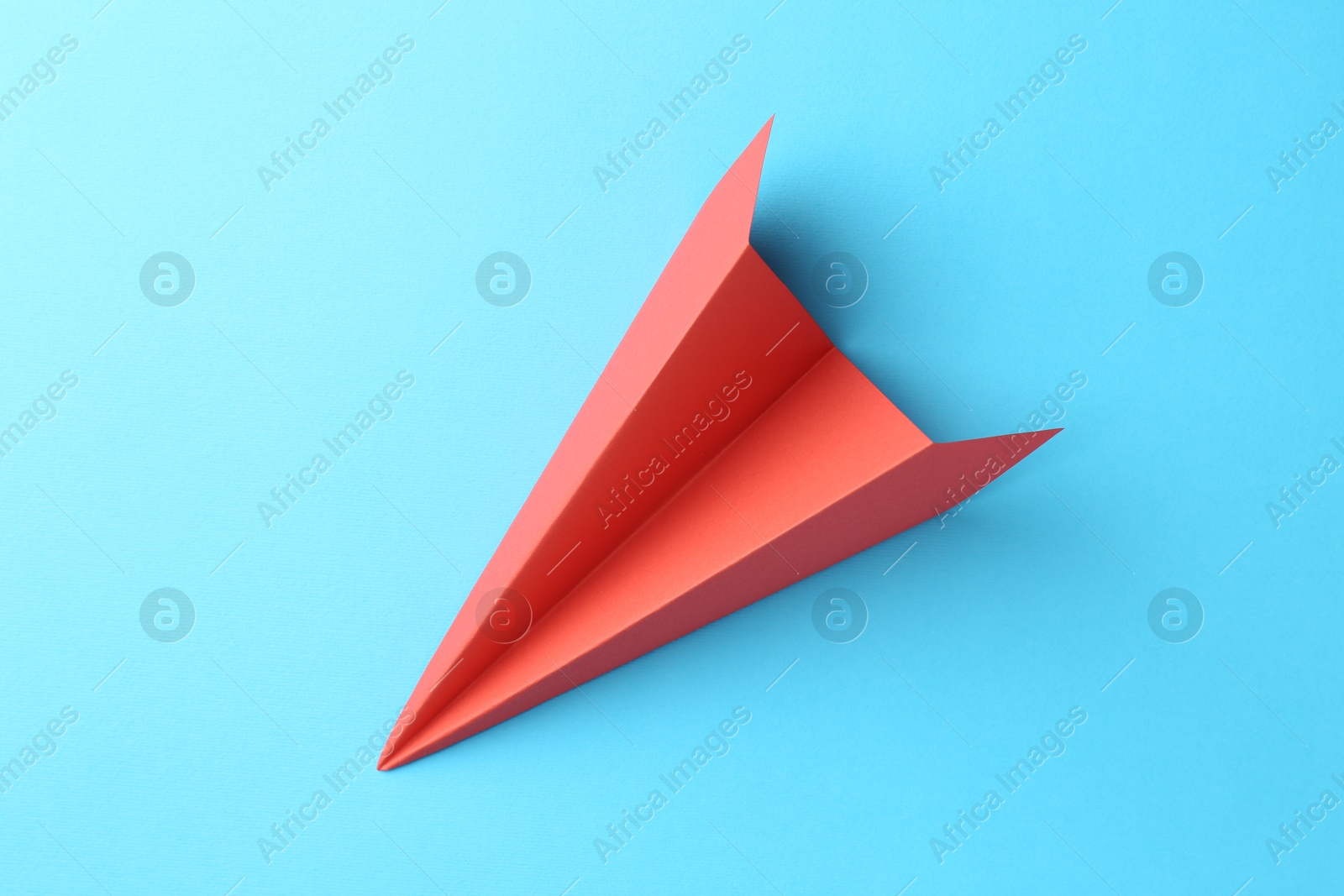 Photo of One handmade coral paper plane on light blue background, top view