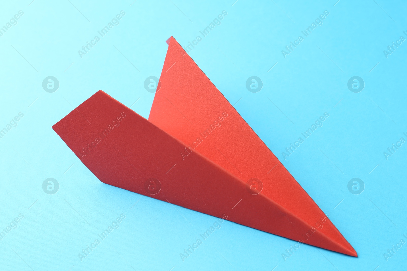 Photo of One handmade coral paper plane on light blue background