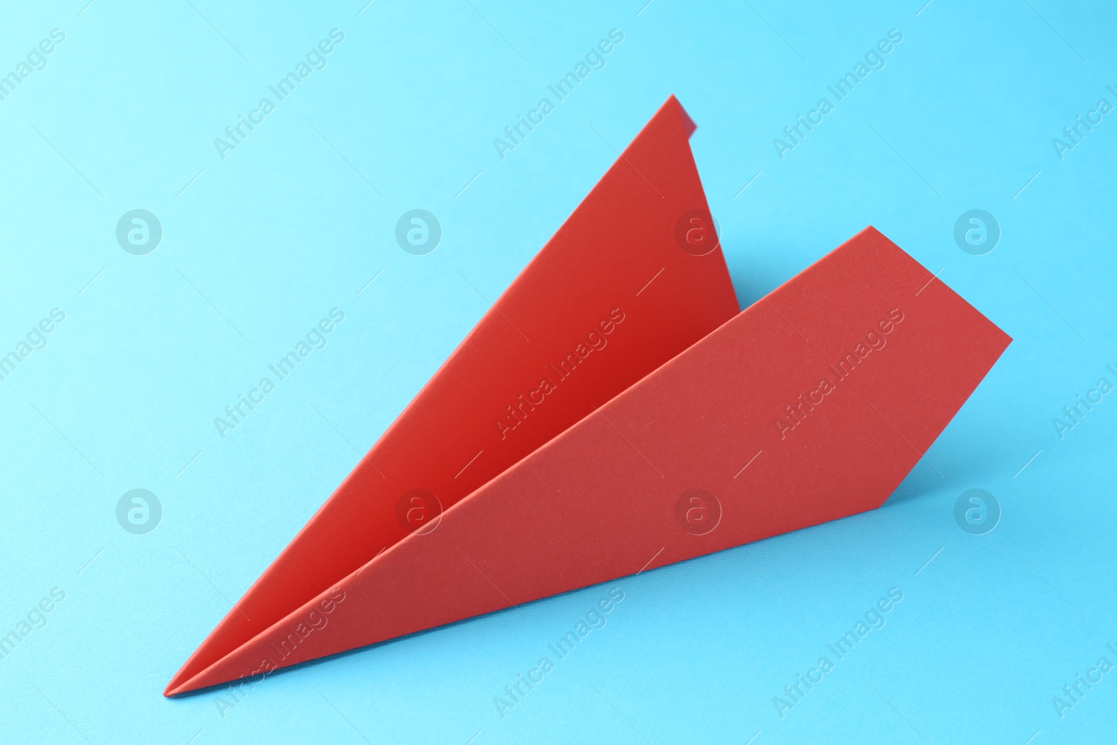 Photo of One handmade coral paper plane on light blue background