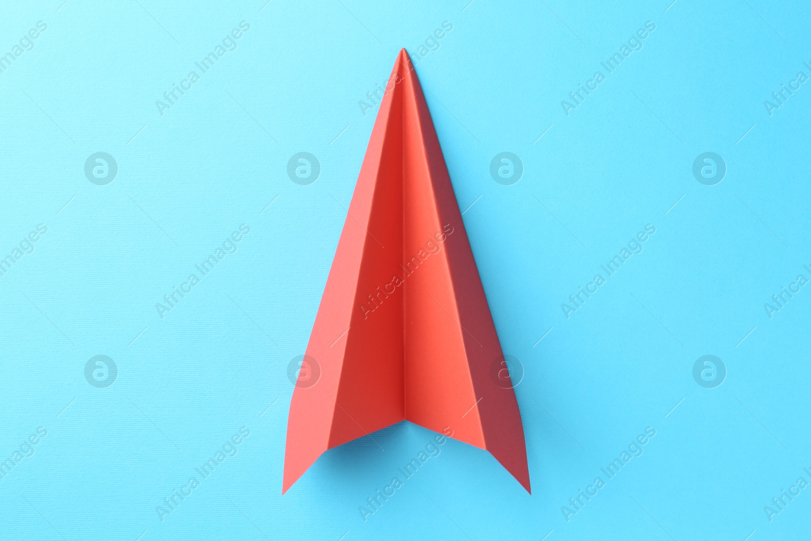 Photo of One handmade coral paper plane on light blue background, top view