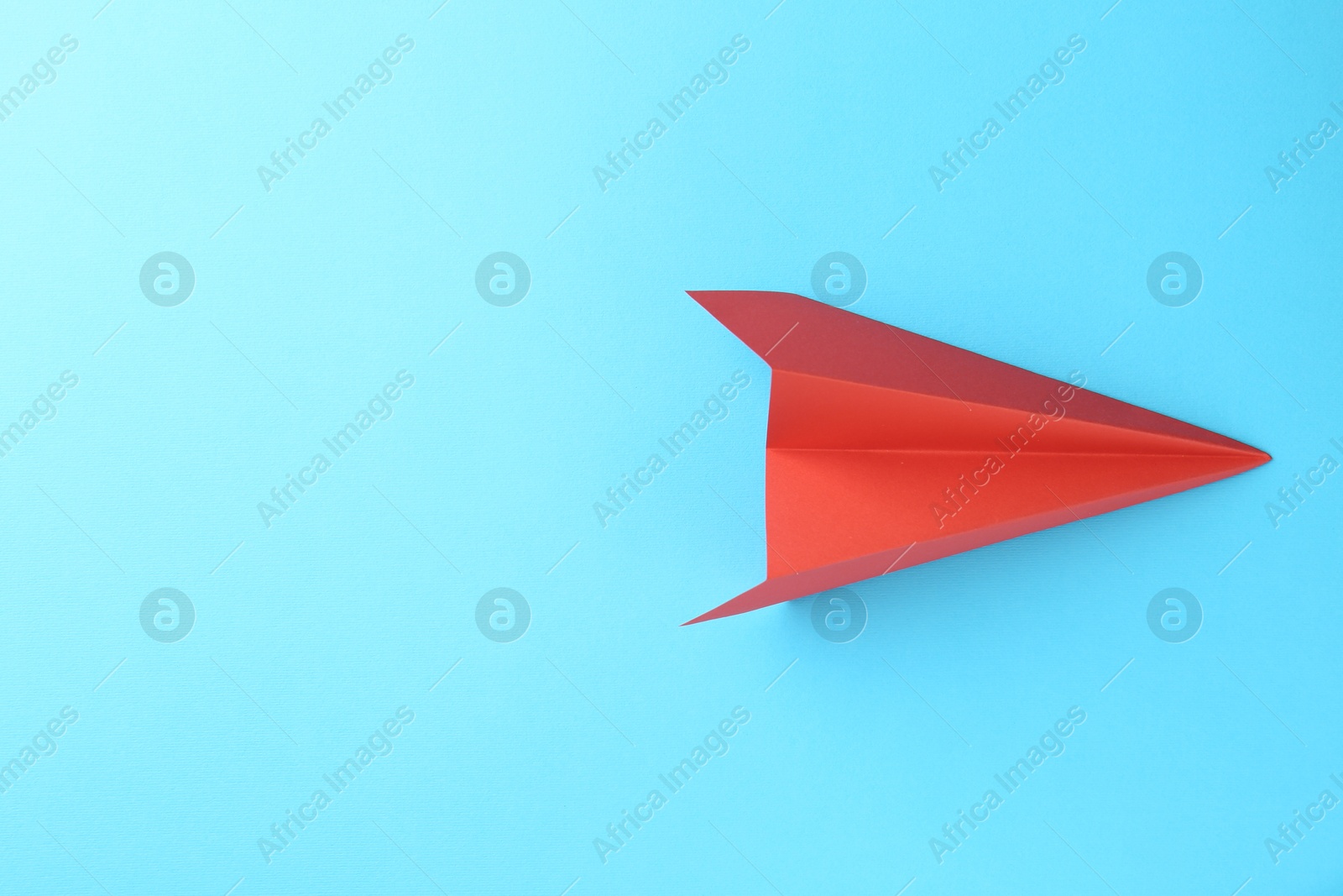 Photo of One handmade coral paper plane on light blue background, top view. Space for text