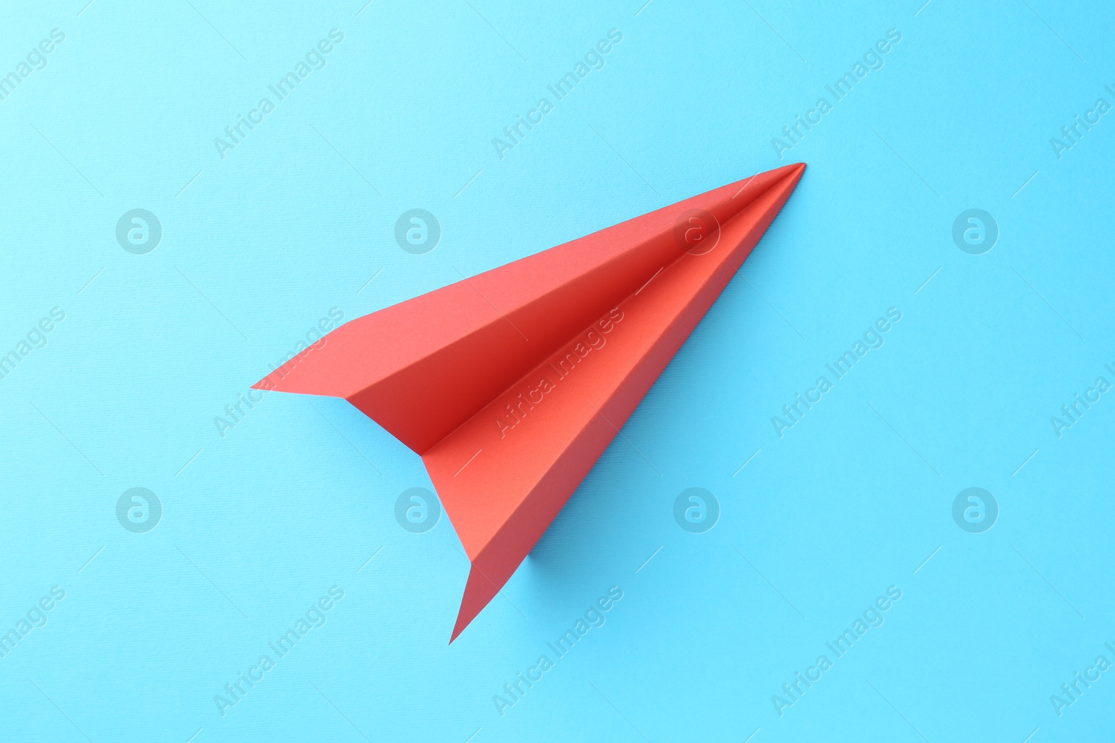 Photo of One handmade coral paper plane on light blue background, top view